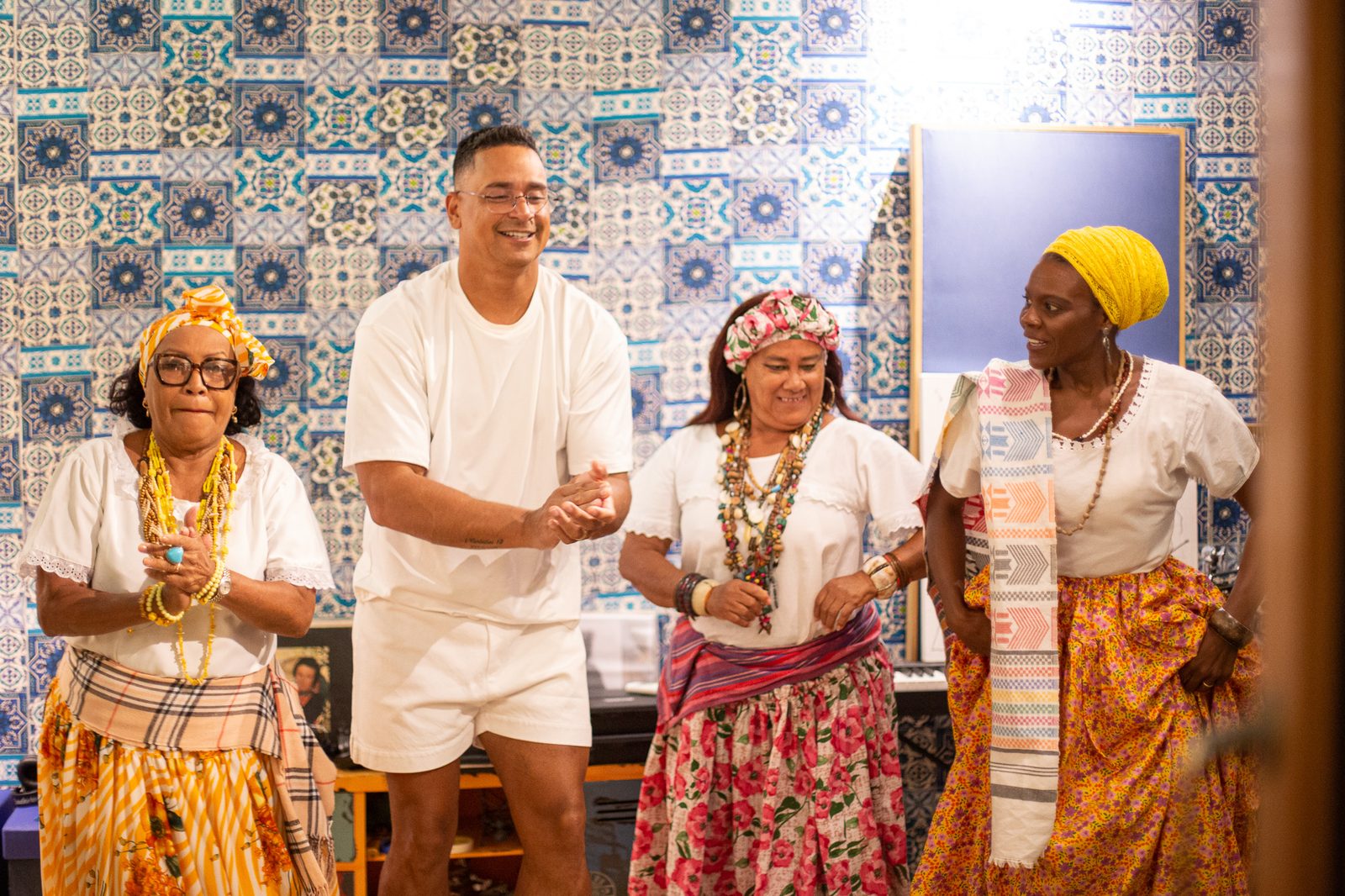 Integrantes das Ganhadeiras de Itapuã cantando e batendo palmas durante a gravação, diante de uma parede de azulejos azuis.